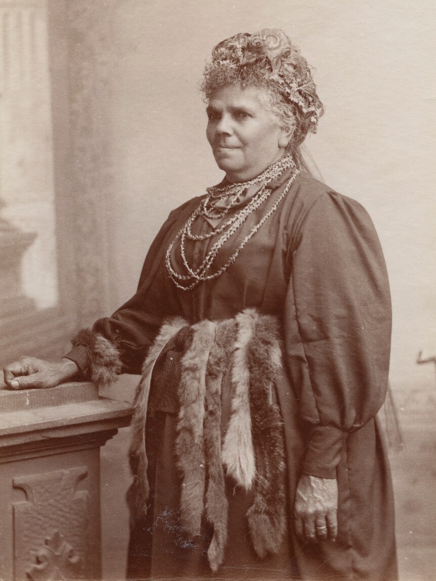 A sepia-coloured photo of an older Fanny, with flowers in her hair and pelts around her waist.