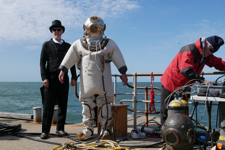 A man in a black suit and top hat next to a man in a historical diving costume 