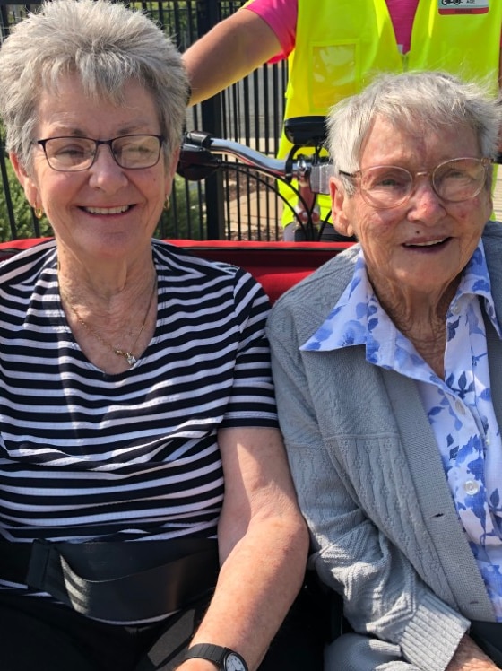 Two aged care residents siti at the front of a special bike that is ridden by a volunteer