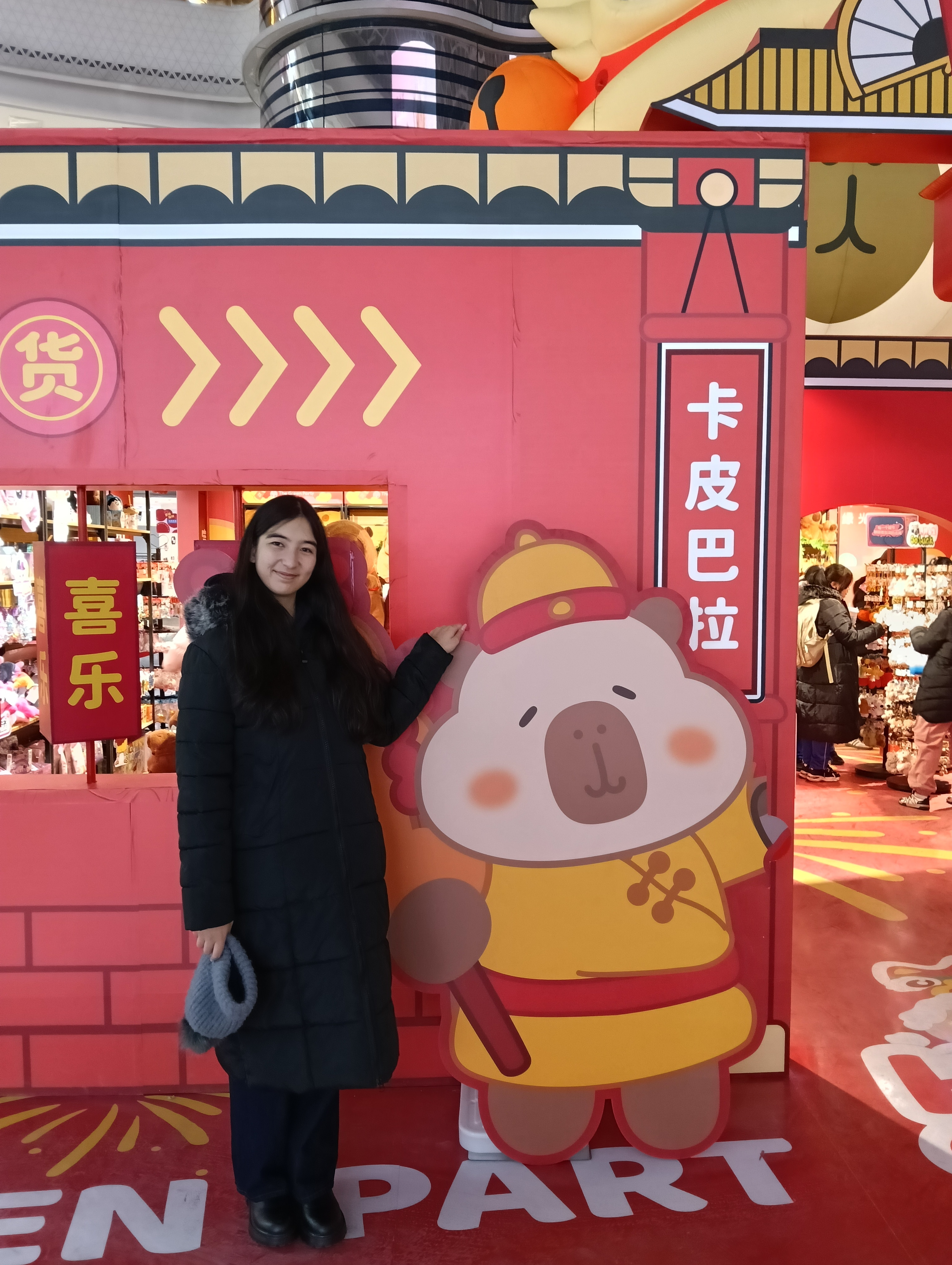 A woman in a black coat stands next to a cartoon bear on a wall