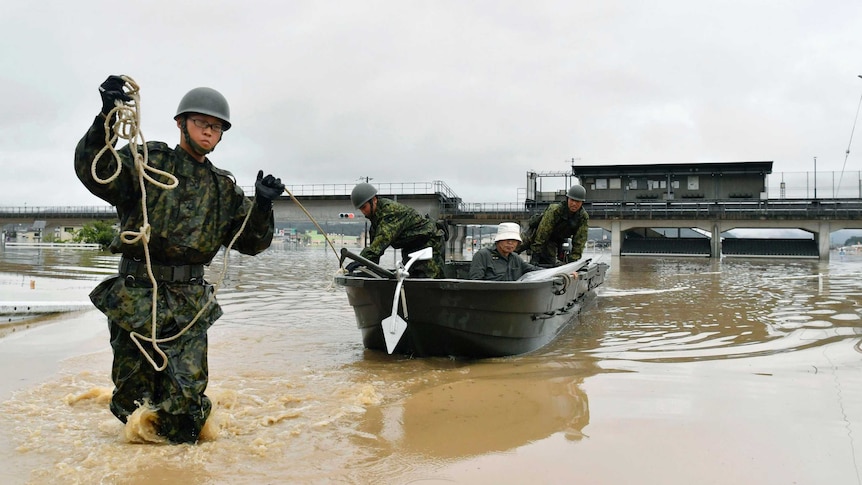 Wide shot of a soldier pulling a boat through floodwaters.