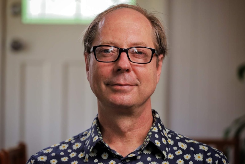 A middle-aged man wearing glasses poses for a portrait looking serious.