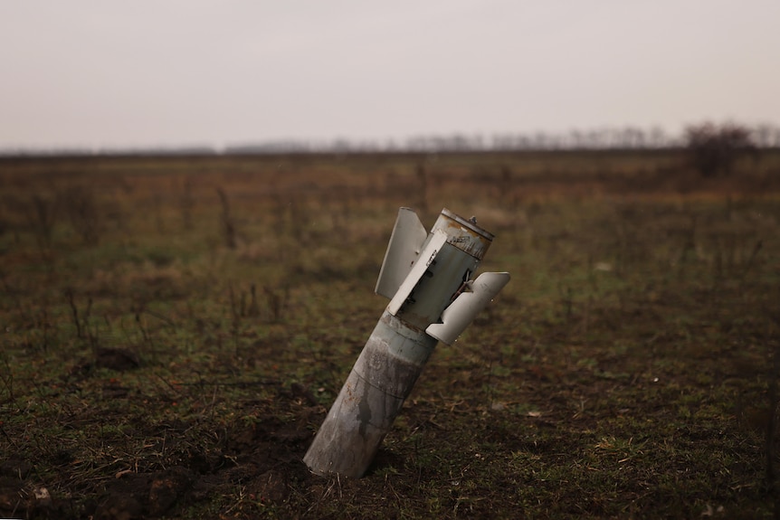 An unexploded rocket sits in the ground in a field. 