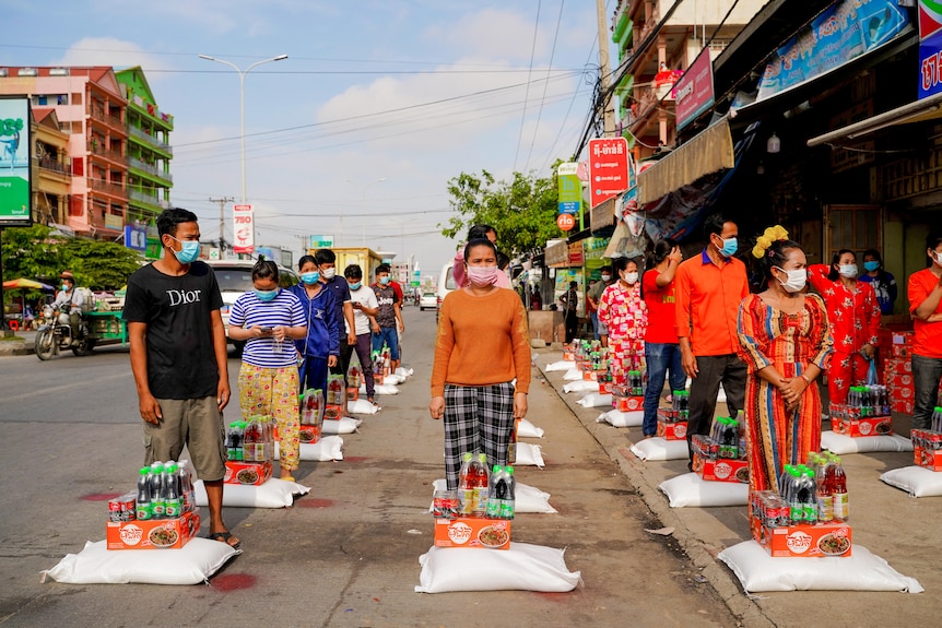 Rows of Cambodians in face masks stand in front of rice bags 