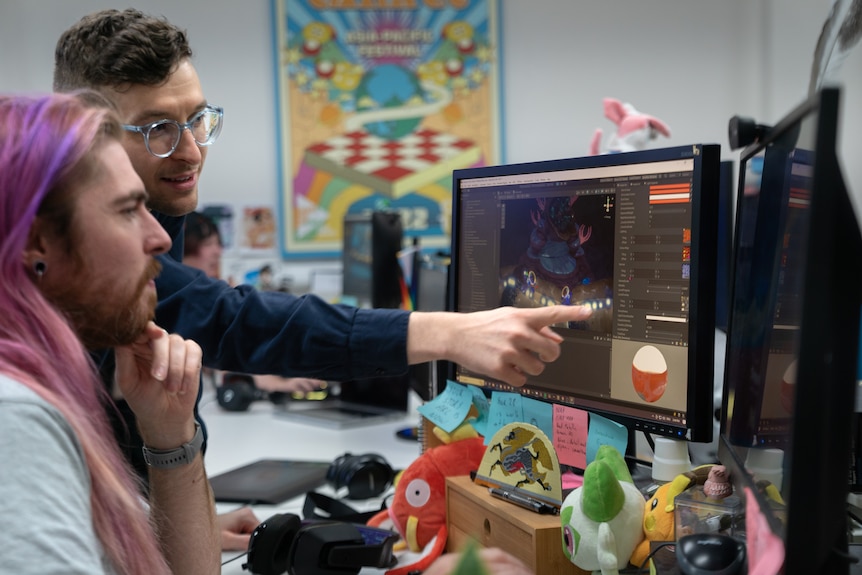 James and a developer sit in front of a computer screen pointing to something on the screen