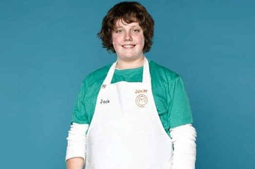 A boy in a chef's apron looks at the camera