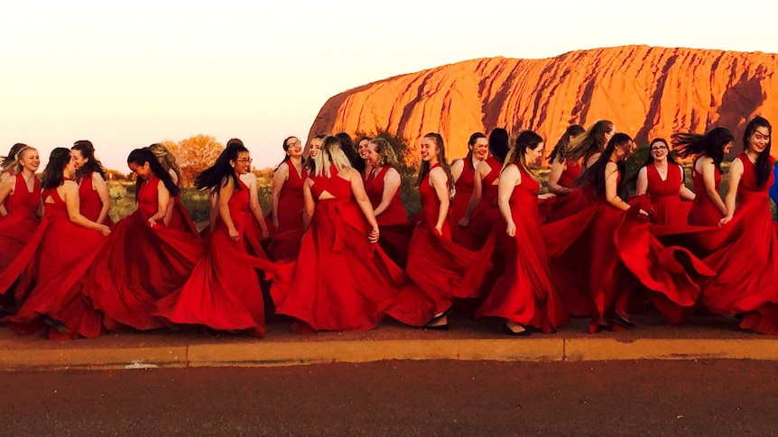The Australian Waratah Girls choir, all wearing red, photographed at Uluru.