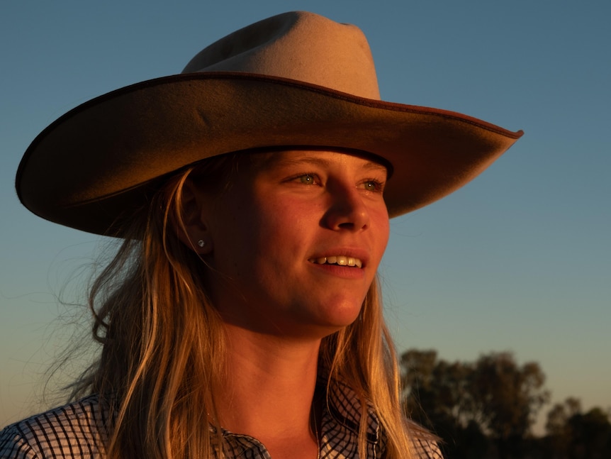 A blonde woman wearing a cowboy hat stares into the sunset