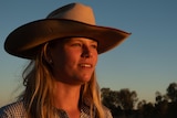 A blonde woman wearing a cowboy hat stares into the sunset