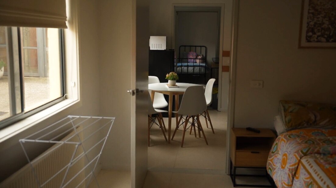 A dining table and chairs seen through the door of a bedroom.