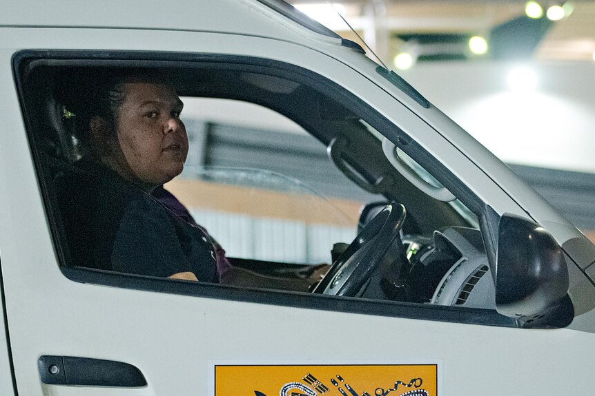 A woman looks serious behind the wheel of a van. 