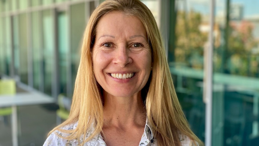 Caucasian woman in her late 50s with ginger blonde hair, brown green eyes, smiling joyfully to the camera.