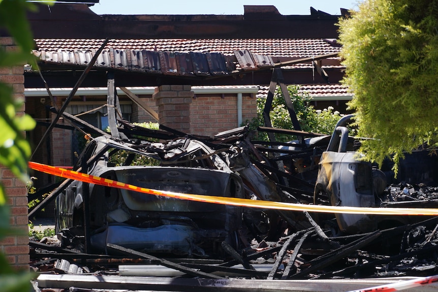 Charred cars sit behind a tape in a garage
