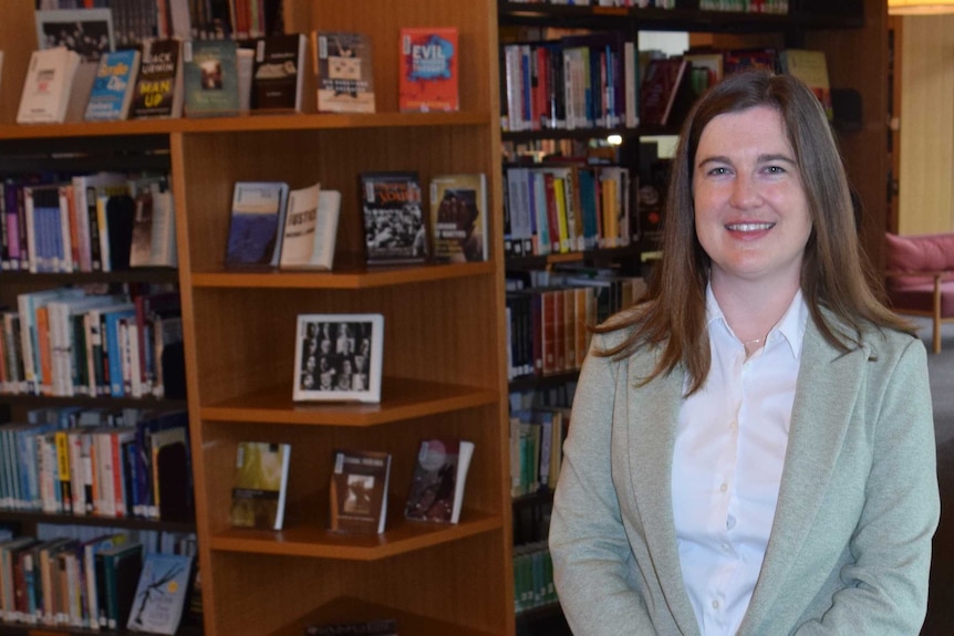 A woman stands in a library in front of books on shelves.