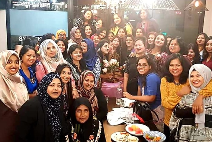 A group of women gather around a dinner table, some wearing head coverings, others not.