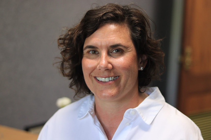 A head shot of a smiling Julia Powles — she has brown hair and is wearing a white open-necked blouse