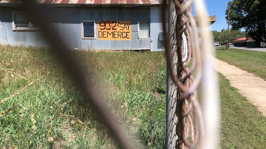 An orange sign reads "93.2% say demerge" on the side of a wall