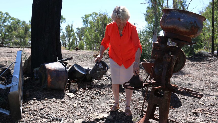 A woman picks up burned pieces of metal.