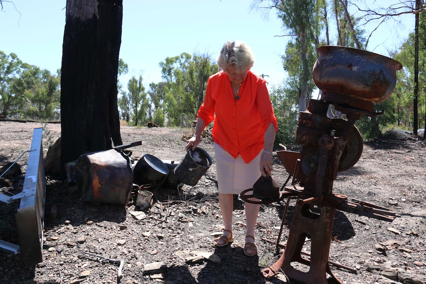 A woman picks up burned pieces of metal.