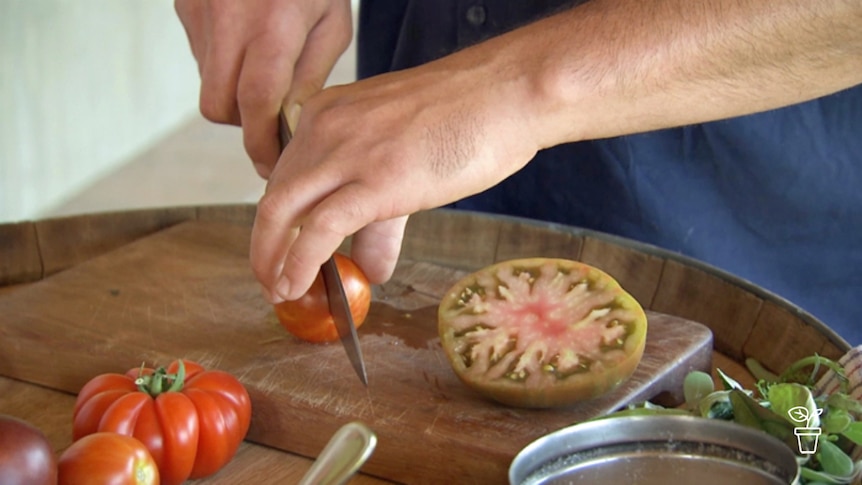 Close up of hand holding knife and slicing tomatoes on wooden chopping board