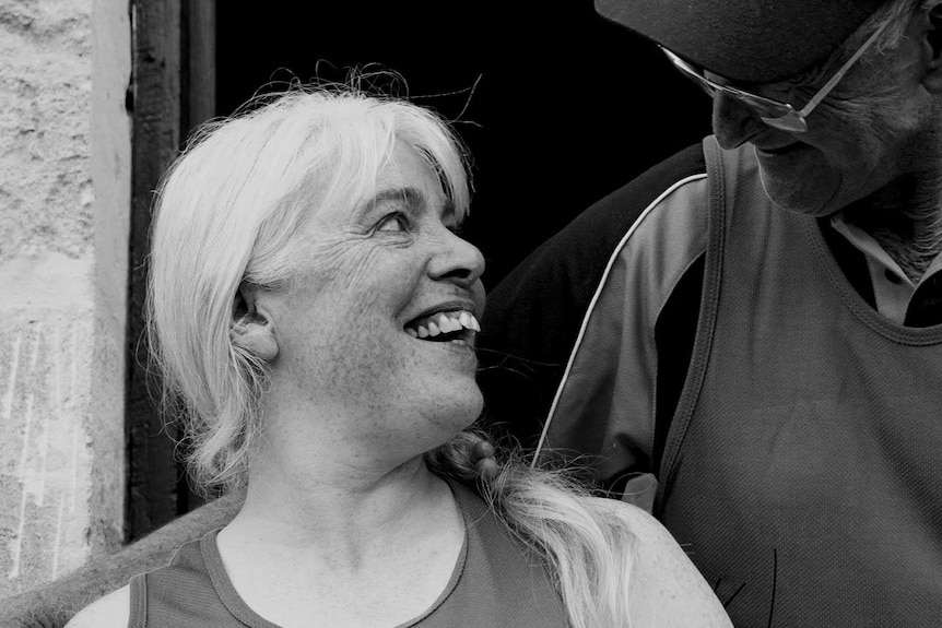 A black-and-white image of a woman smiling at another person at a shearing shed