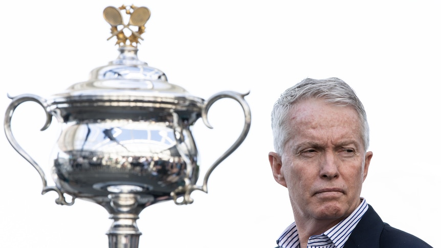 Craig Tiley looks to his left with an Australian Open trophy in the foreground.