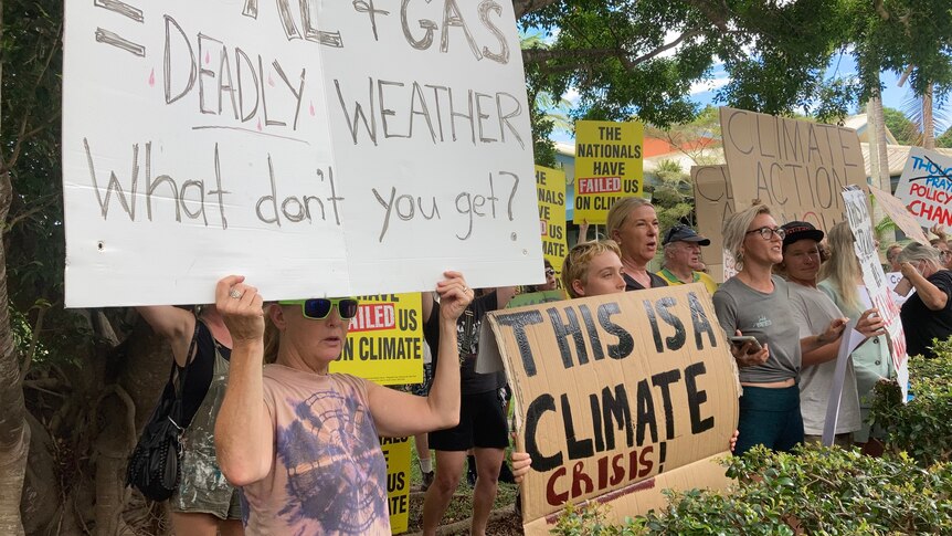 People stand in a line holding signs referring to a climate crisis and government inaction.