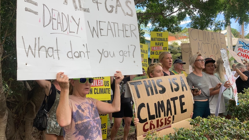 People stand in a line holding signs referring to a climate crisis and government inaction.