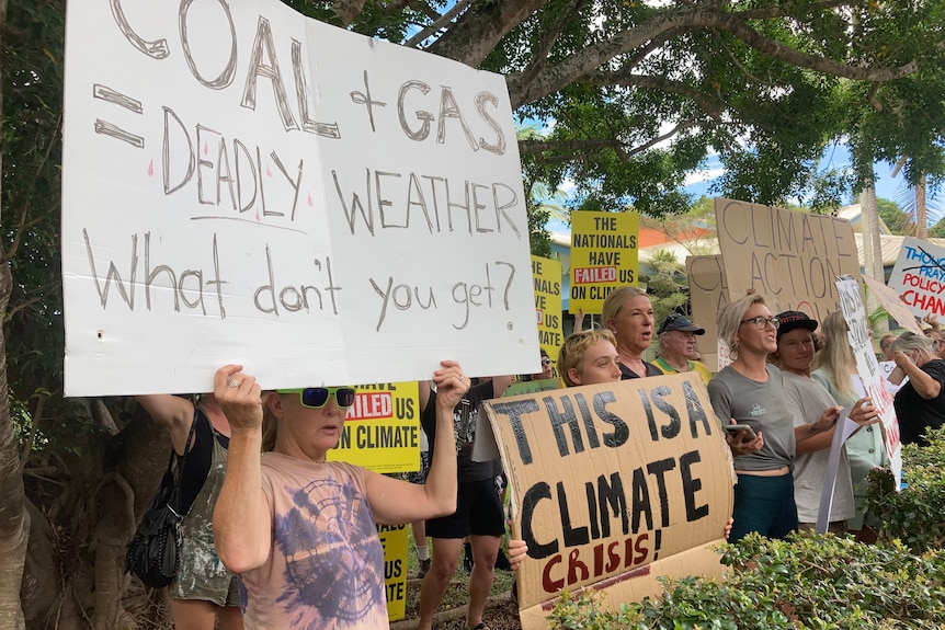 People stand in a line holding signs referring to a climate crisis and government inaction.