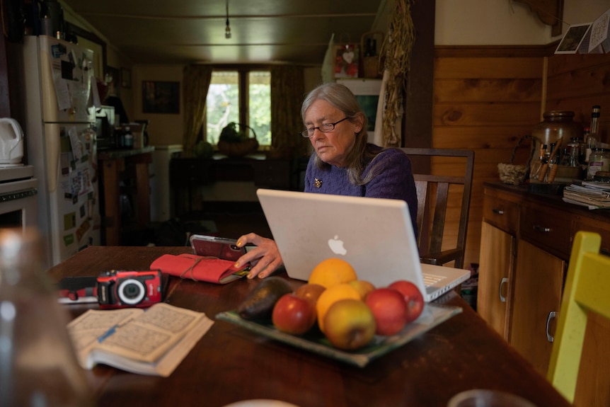 A woman looks at her phone while her laptop sits open on the table.