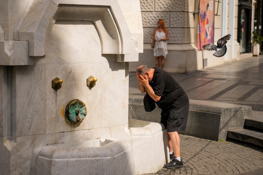 Man cools himself off by throwing water on his face at a public fountain. 