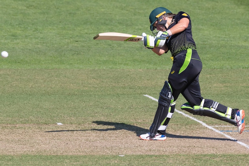 A female cricketer watches the ball on her follow through after hitting it down the ground.
