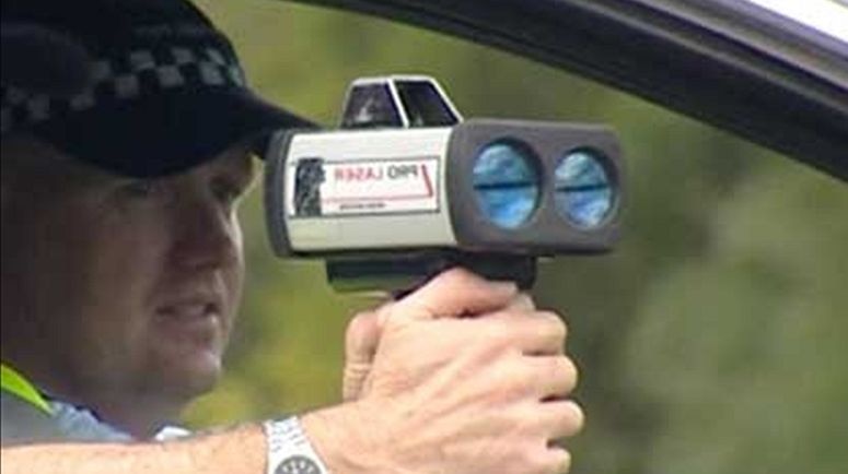 A police officer holding a radar speed camera in a car