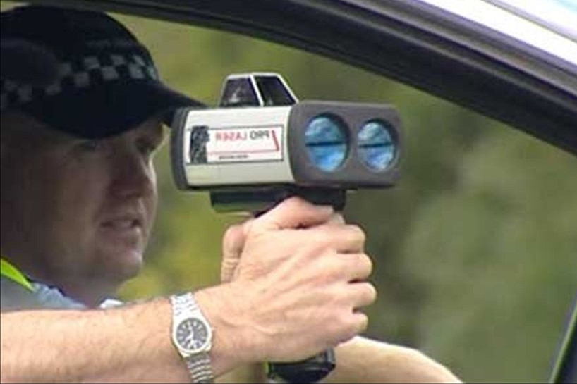A police officer holding a radar speed camera in a car