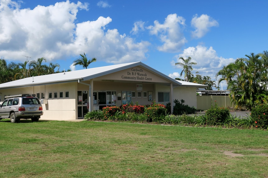 A cream-coloured building set back behind a large green lawn, with a blue sky in the background.