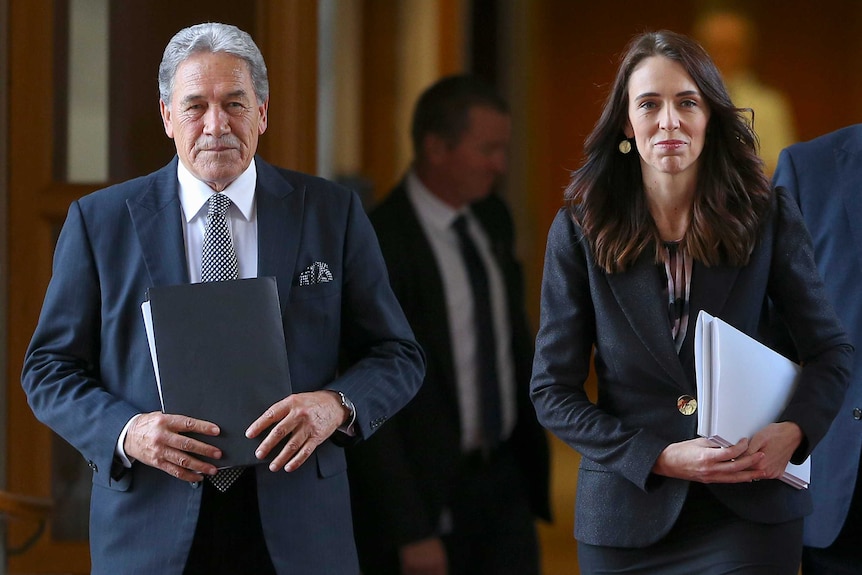 Jacinda Ardern walks with Winston Peters, both clutching papers and staring ahead.