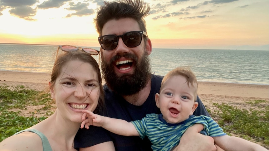 A selfie of a woman, man and young child on the beach during sunset. 