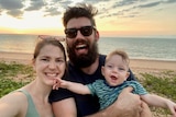 A selfie of a woman, man and young child on the beach during sunset. 