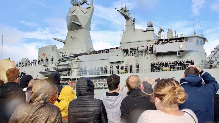 People look up at a navy ship.