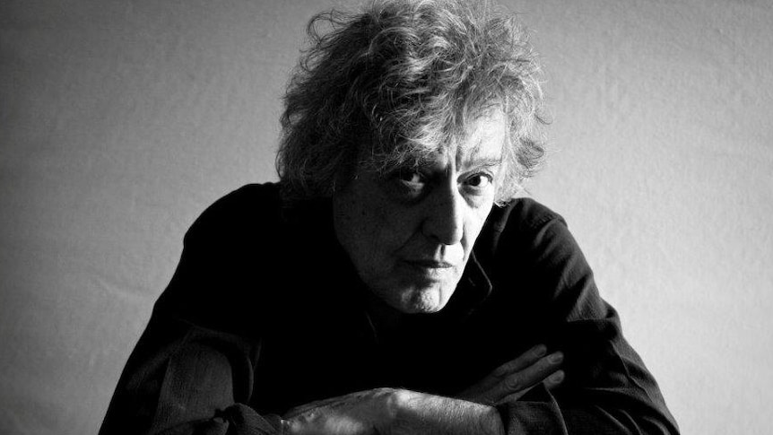 A black and white portrait of Tom Stoppard leaning forward with his arms folded.