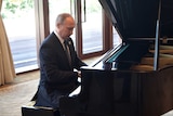 Russian President Vladimir Putin looks at the keys as he plays a piano.