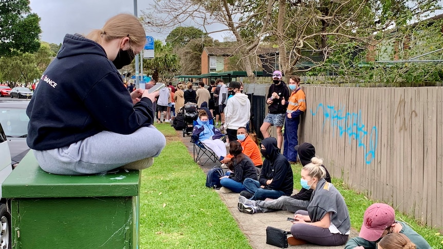 A lone line of people in face masks waiting on the street.