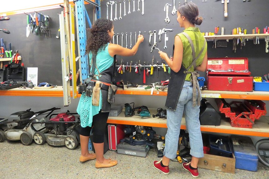 Sabrina Chakori and Samantha Wigman put tools back in rack mounted on wall.