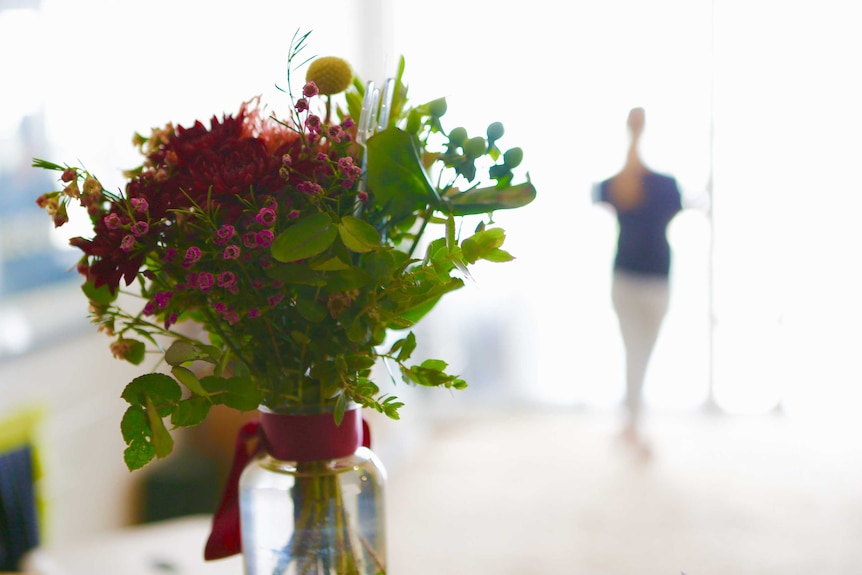 Flowers in a vase with a woman standing in the background