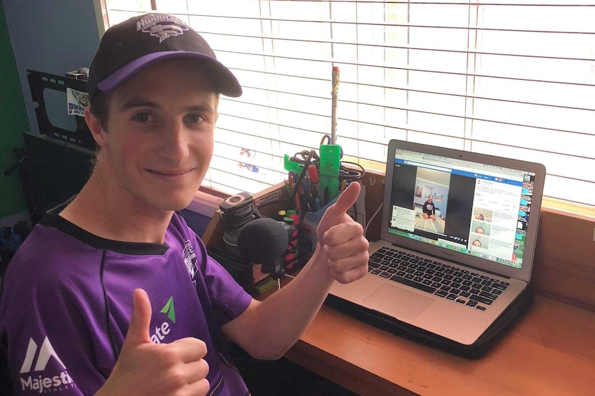 Jacob Bevis sitting at his desk with his back turned to his computer as he gives the thumbs up.