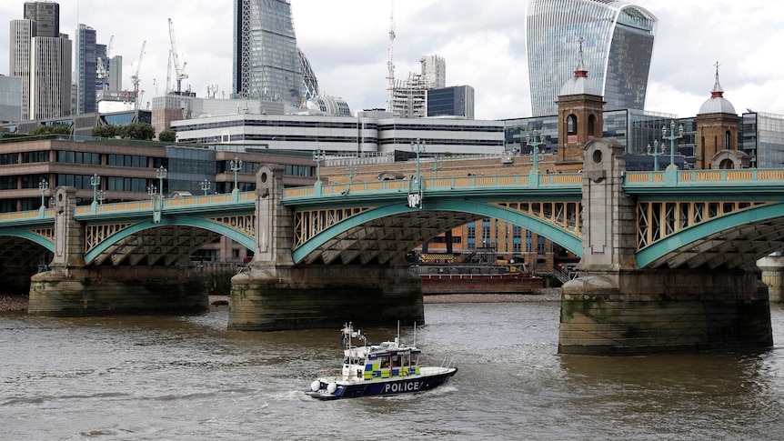 A police boat heads under Southwark Bridge on the River Thames towards London Bridge.