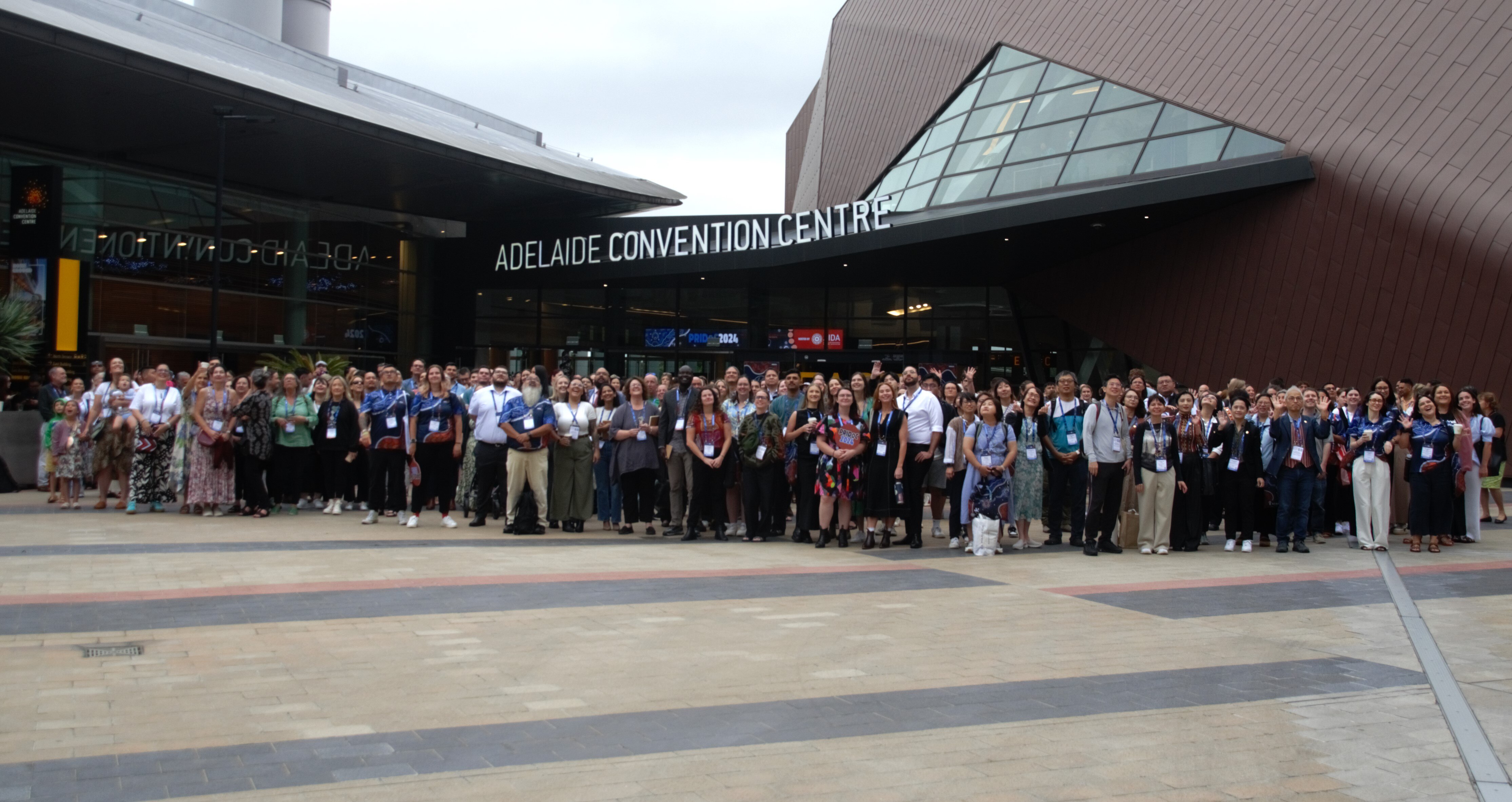 A large group stands outside a building signed 'ADELAIDE CONVENTION CENTRE'