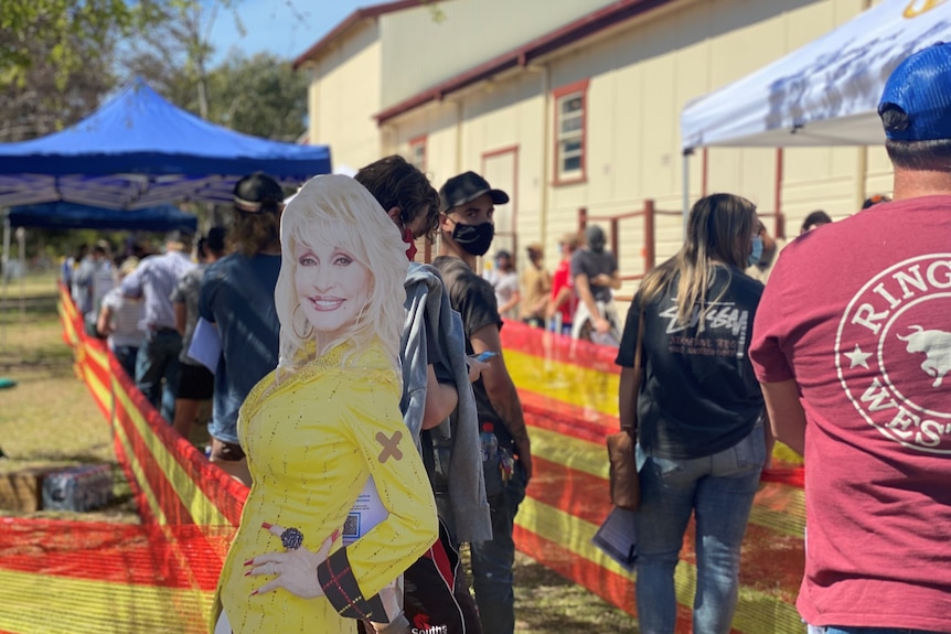 A cardboard cut out of Dolly Parton in front of a queue of people