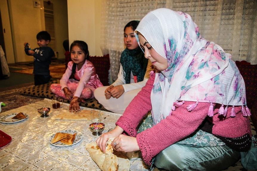 A woman sitting on a mat in a lounge room enjoys  naan bread with two children nearby