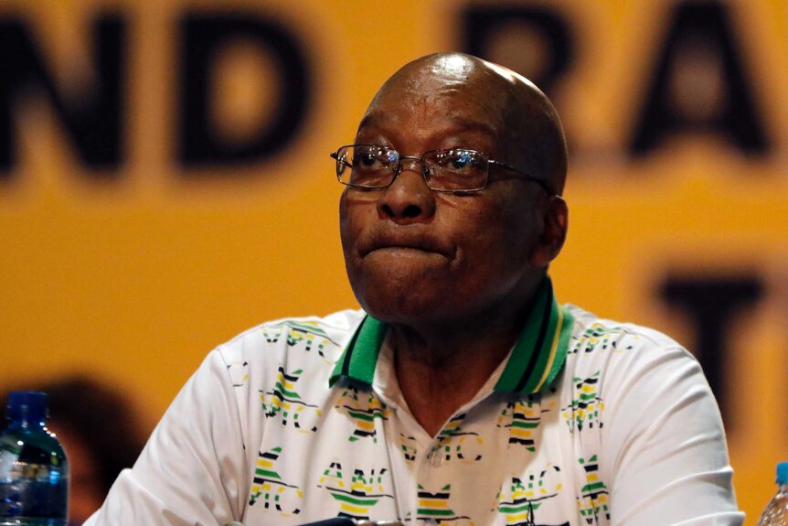 Jacob Zuma sits at a table with a disappointed look on his face.